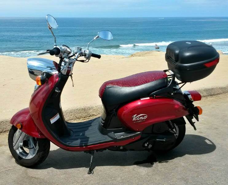 Ruby Garnet Gator seat cover fitted to a red Yamaha Vino 125 beside the ocean, handmade by Cheeky Seats.