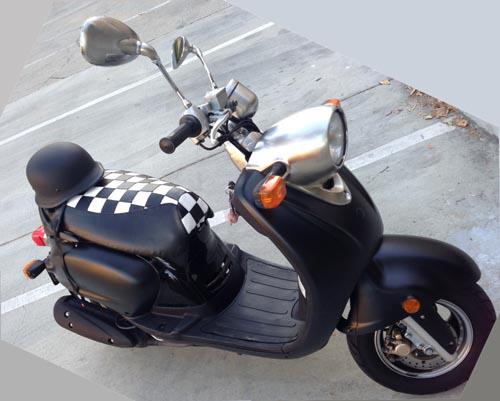 Black-and-white Checkers seat cover fitted to a black Yamaha Vino 125, adding a graphic racing accent, handmade by Cheeky Seats.