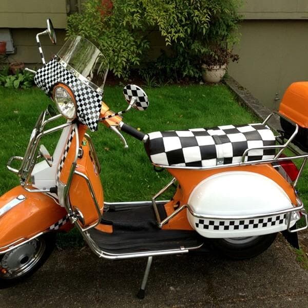 Orange Genuine Stella fitted with a black-and-white checker Cheeky Seats cover and matching scooter accents