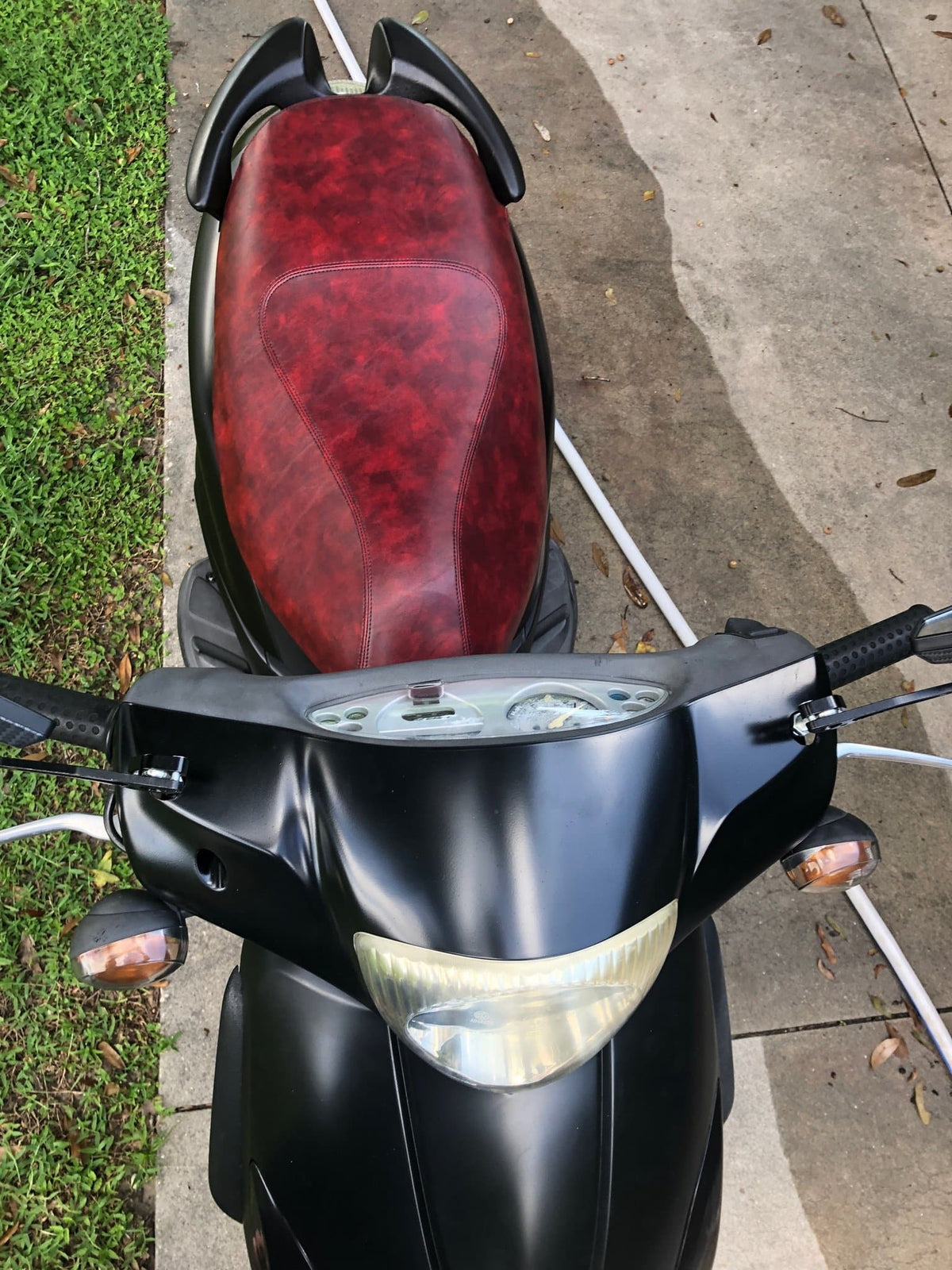 Overhead rider view of an oxblood marbled seat cover installed on a black Piaggio Fly scooter, handmade by Cheeky Seats