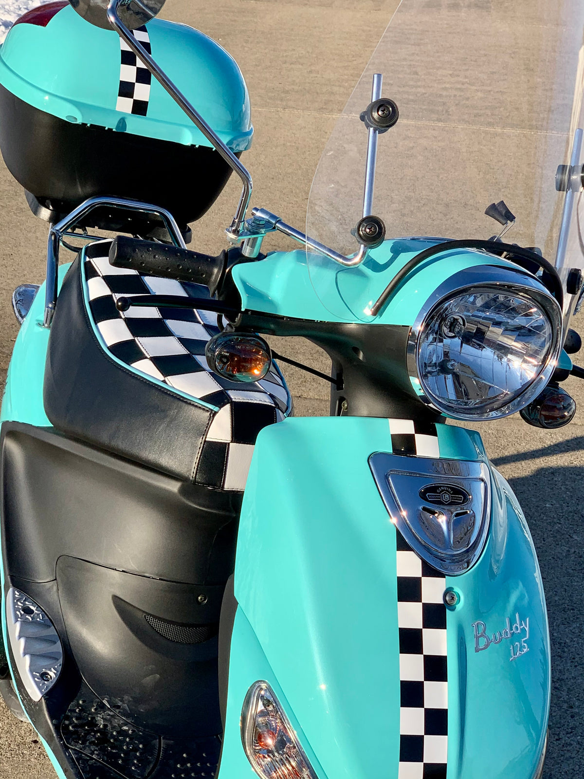 Turquoise Genuine Buddy 125 with a black-and-white checkered Cheeky Seats cover, overhead front view