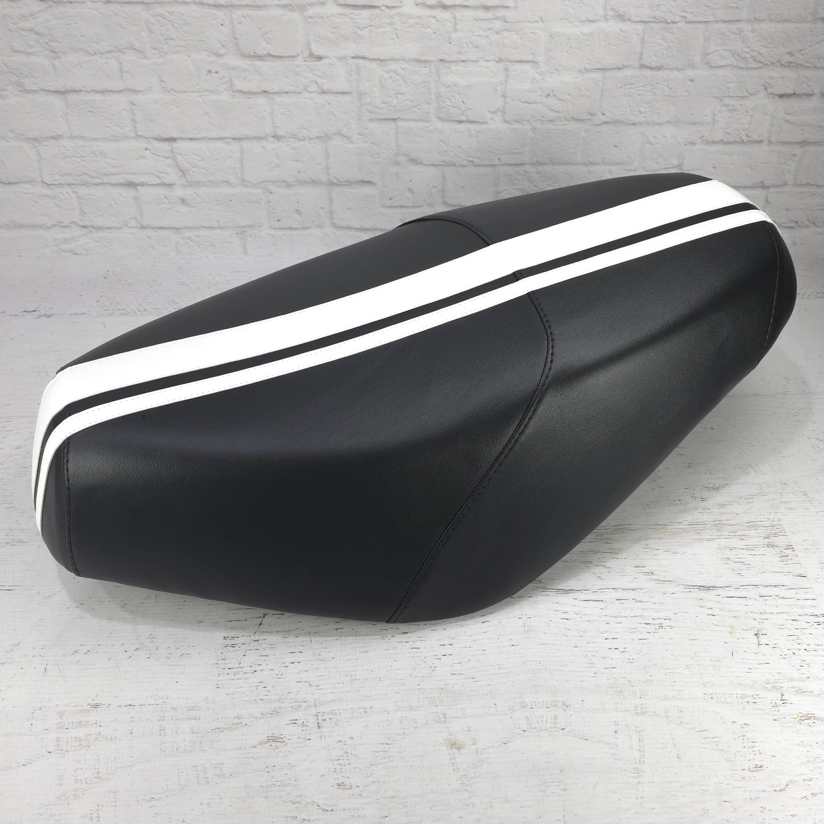 Dual white racing stripes running over a black Cheeky Seats Genuine Buddy cover, left-side studio view