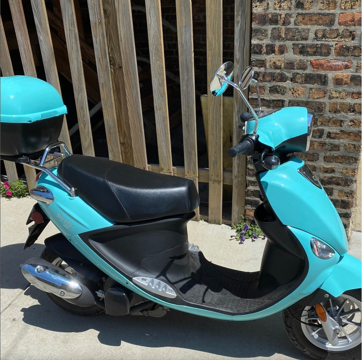 Turquoise Genuine Buddy scooter with a fitted classic black Cheeky Seats cover, right-side view