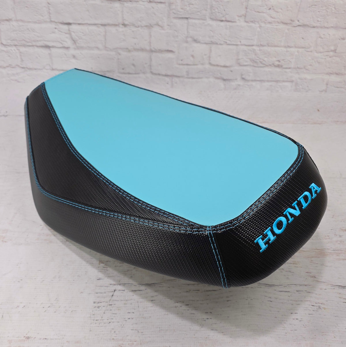 Honda Dio 1 & 2 Aqua Blue Two Tone Seat Cover with black carbon fiber sides and a blue embroidered Honda logo, handmade seat cover by Cheeky Seats