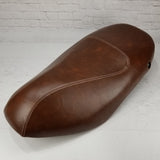 Whiskey brown Piaggio Fly 50–150 seat cover with cream French seams and a fitted lock opening, handmade by Cheeky Seats