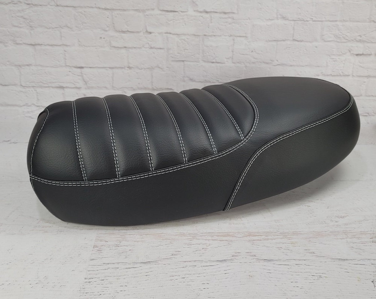 Rear side view of a black Yamaha Zuma II BWS 49/50 Prebug seat cover showing padded tuck-and-roll channels and gray stitching, handmade by Cheeky Seats