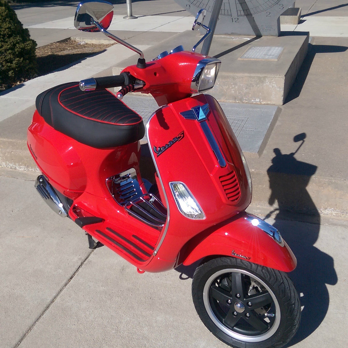 Black tuck-and-roll seat cover with red piping installed on a red Vespa S, handmade by Cheeky Seats