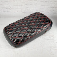 Satin black diamond-stitched Maddog seat cover with red contrast stitching and a glossy wet-look sheen, three-quarter overhead view, handmade by Cheeky Seats
