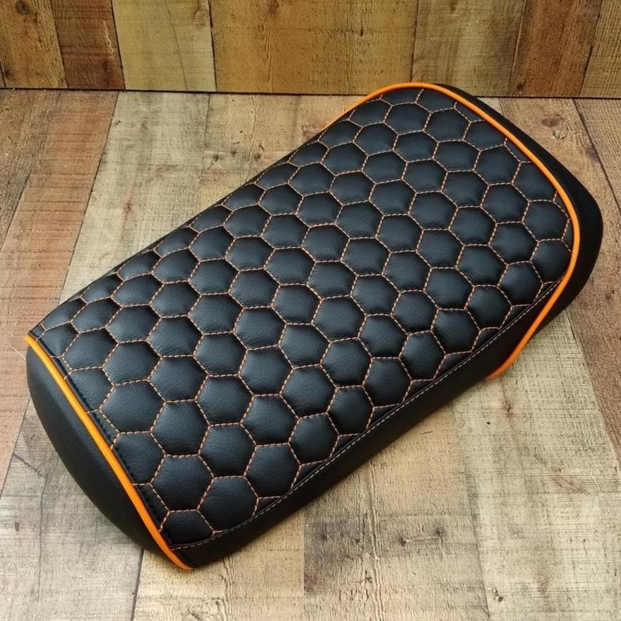 Black hexagon honeycomb seat cover with orange contrast stitching and orange piping against a wood plank backdrop, handmade by Cheeky Seats