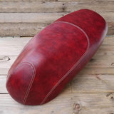 Rich mottled oxblood Kymco Like seat cover on weathered wood planks, overhead angle with cream contrast stitching along the center panel and side seams, handmade by Cheeky Seats
